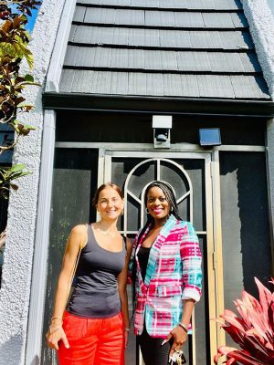 two-woman-front-of-gray-house